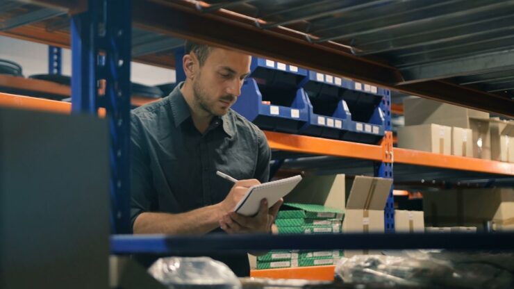 Inventory supervisor conducting manual stocktaking in a storage unit filled with small wholesale items
