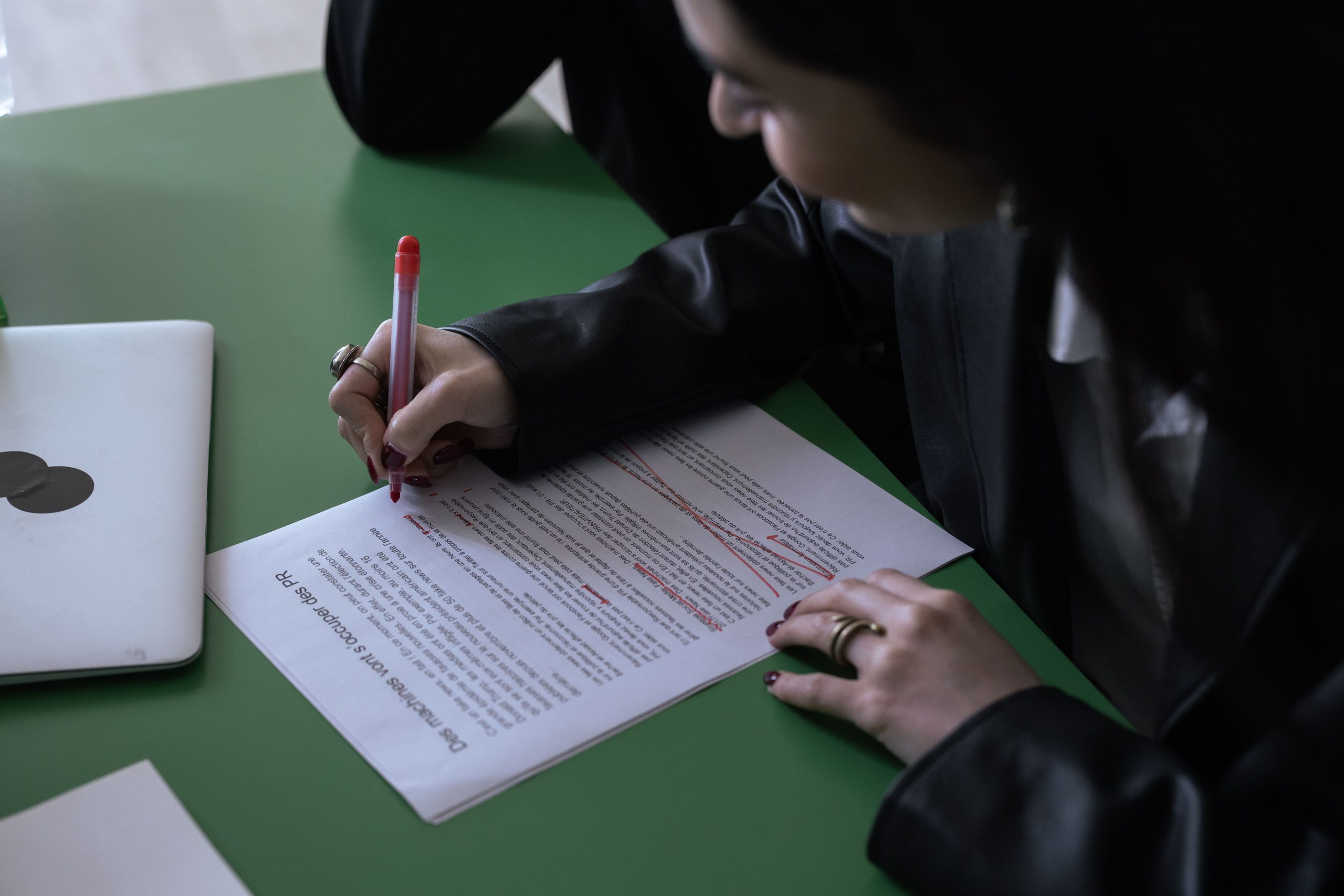 Business professional editing a printed document with a red pen while working alongside a laptop