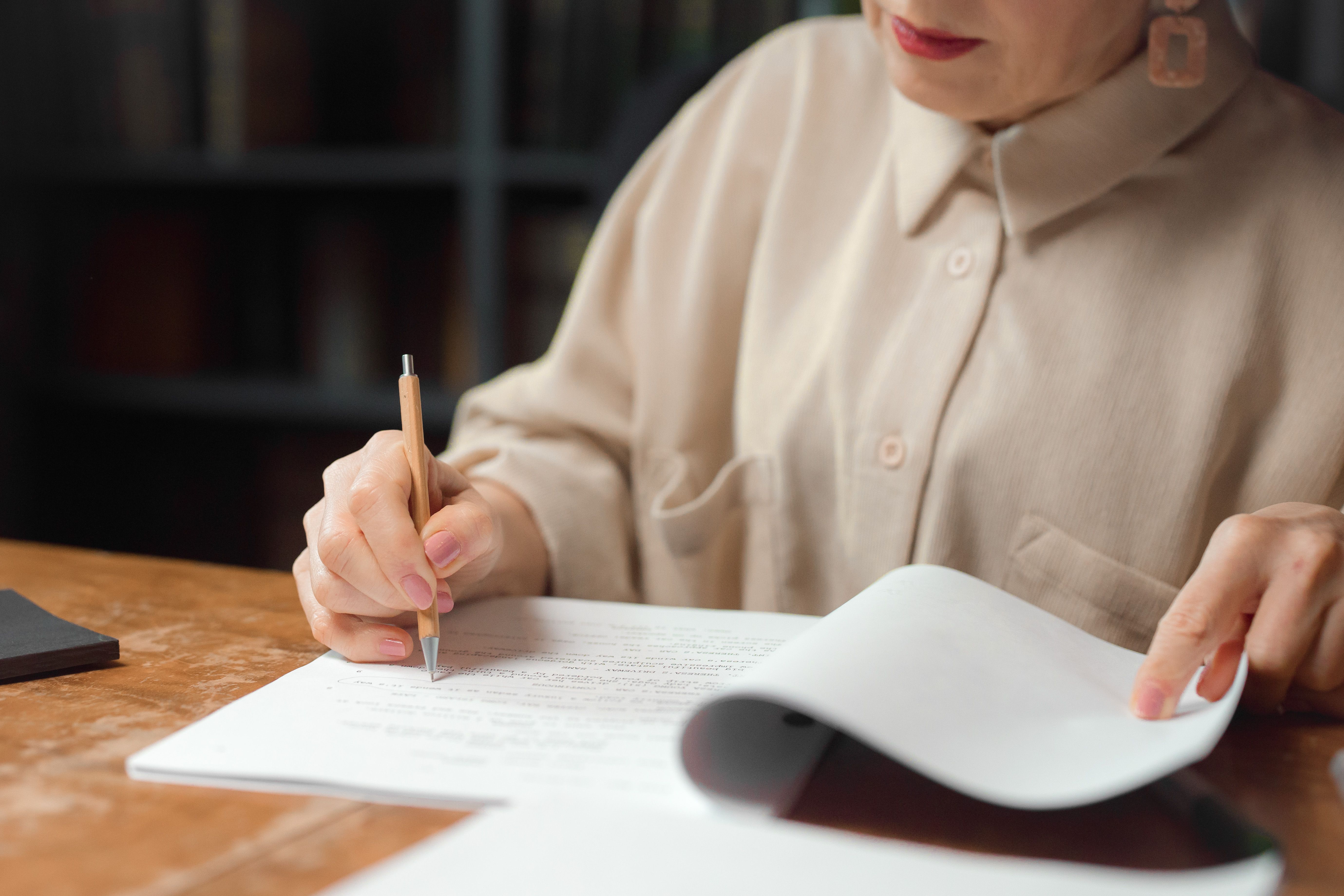 Woman proofreading and reviewing documents at a wooden desk