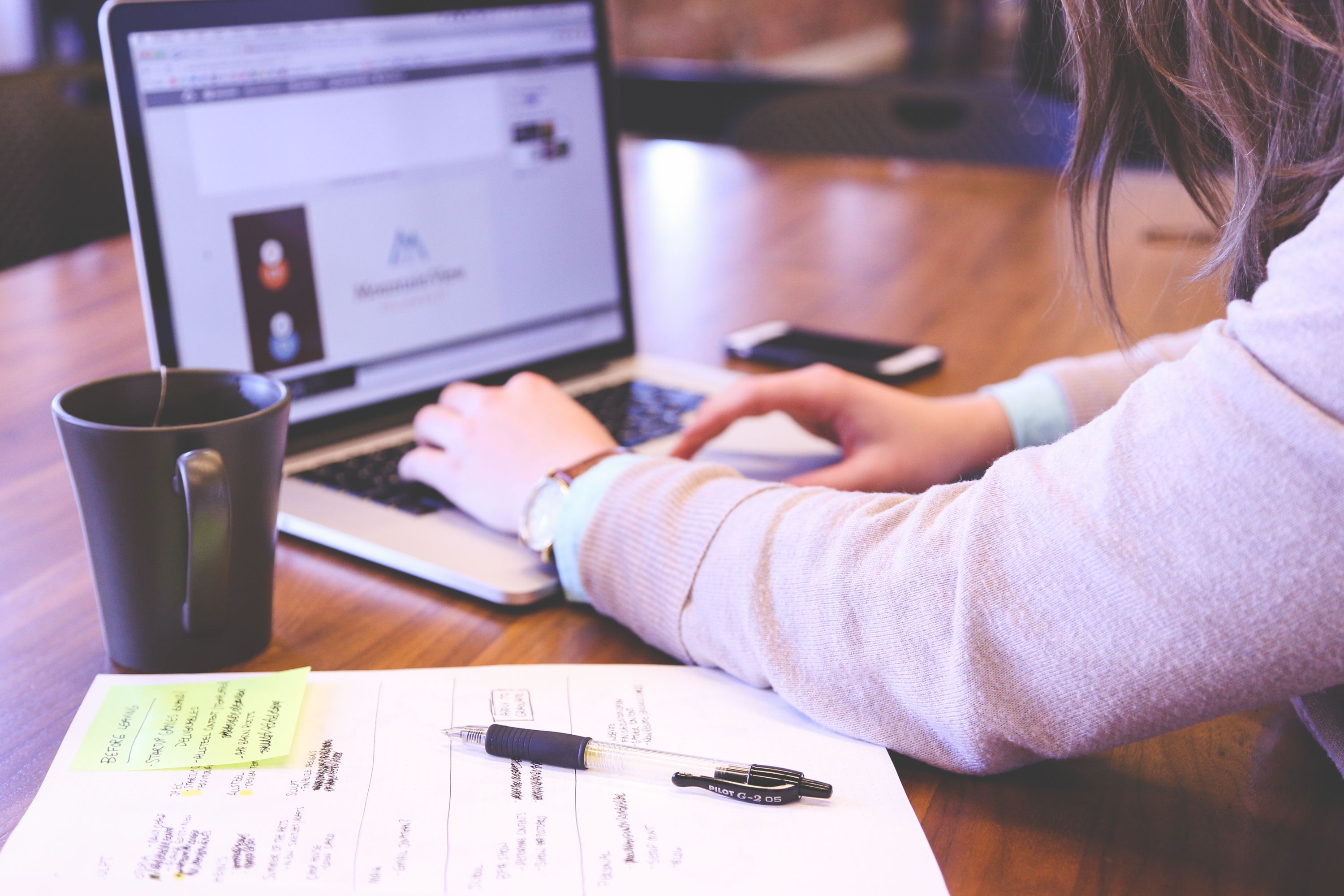 Businesswoman typing on a laptop with notes and coffee on a wooden desk