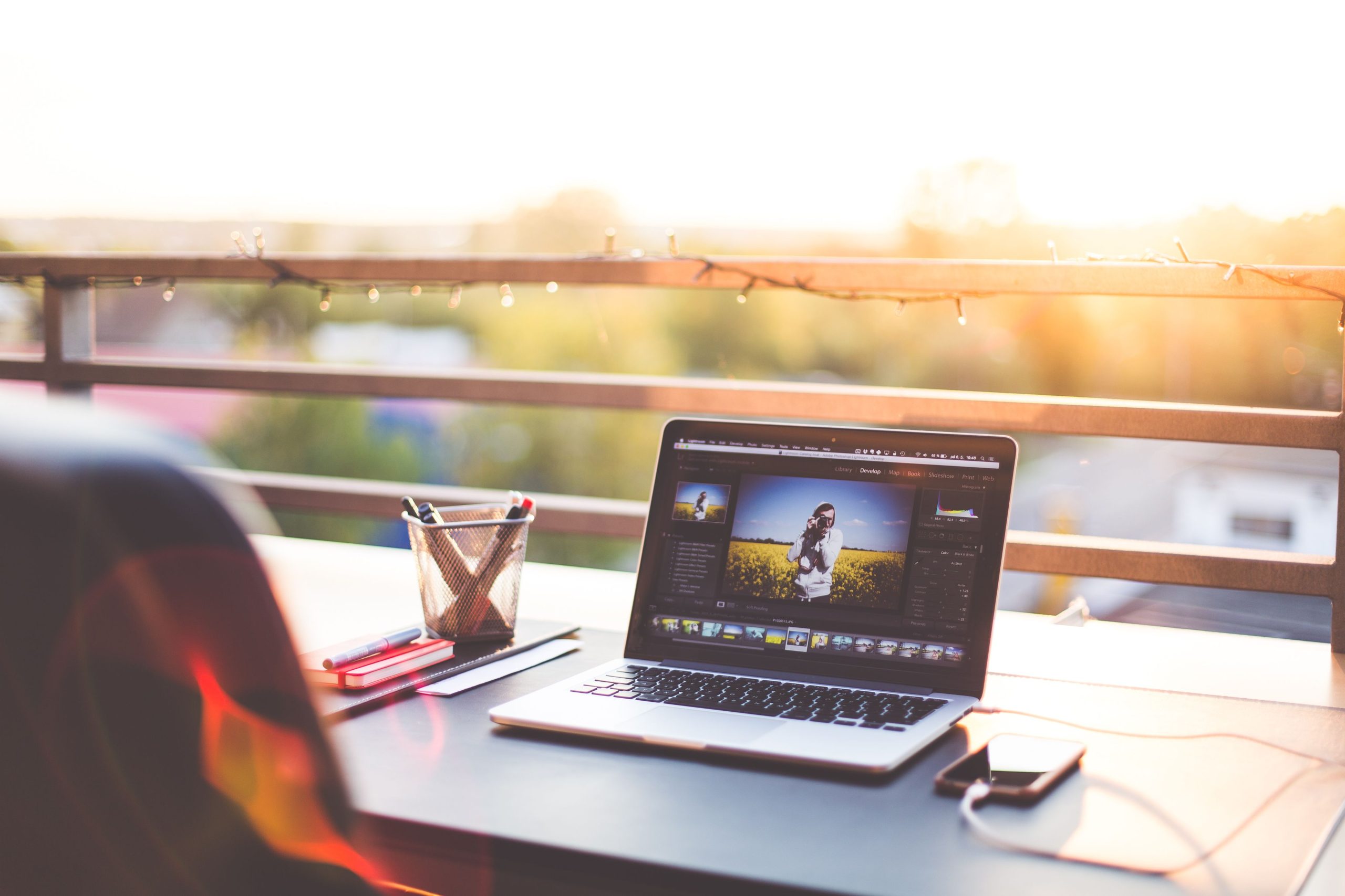 A modern workspace on a balcony with a laptop and smartphone during sunset