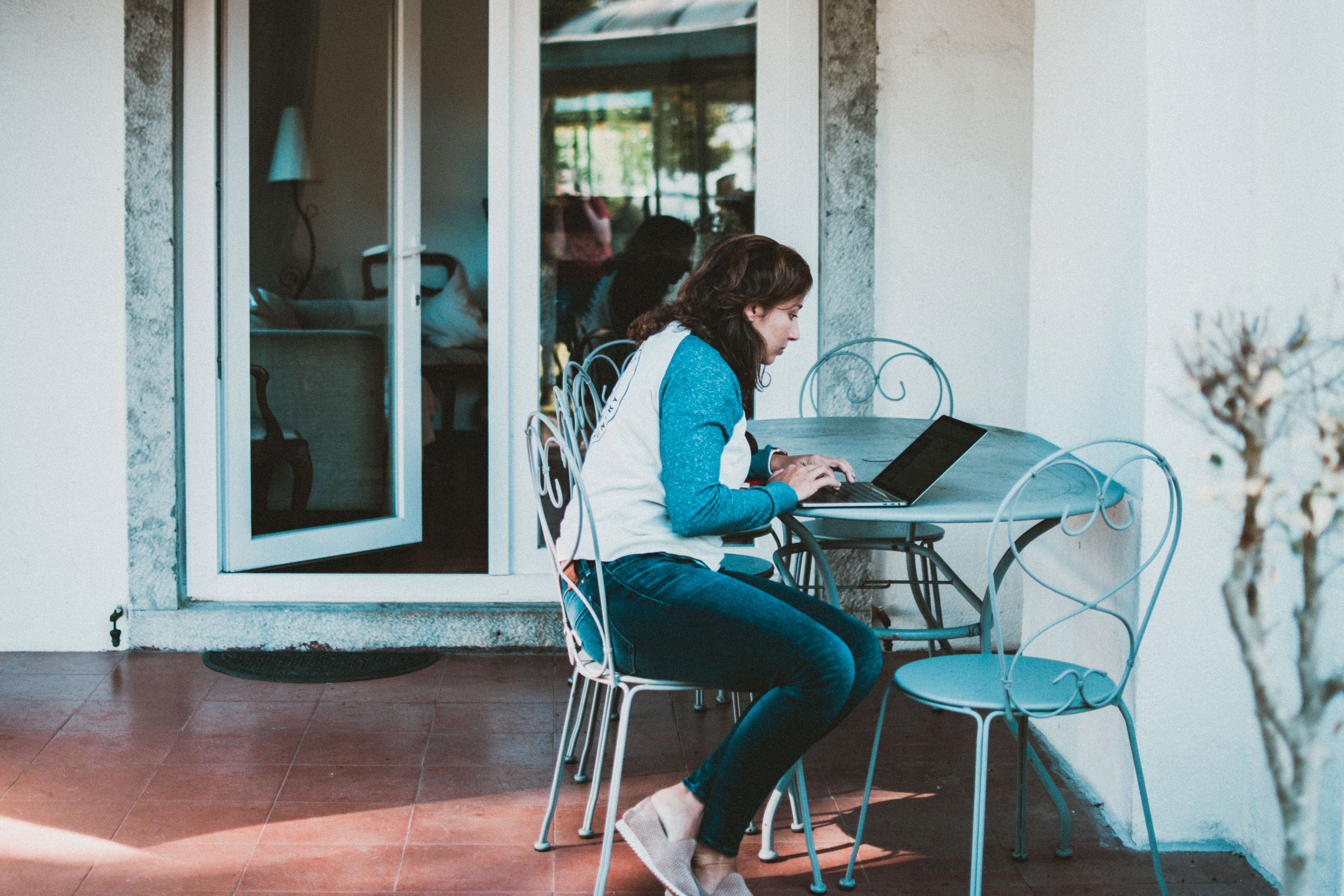 Young woman working on a laptop at a stylish patio table outside a home